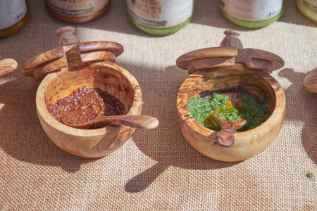 Two handcrafted wooden bowls sit on a burlap surface filled with flavorful sauces. The vibrant colors highlight the skill of local makers as sunlight creates an inviting atmosphere.の写真素材
