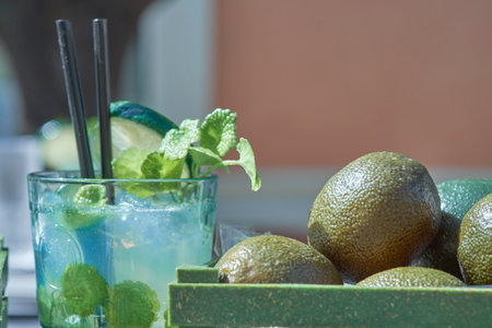 A refreshing mojito sits beside a wooden tray filled with ripe avocados, garnished with fresh mint and lime, creating a vibrant atmosphere at a social outdoor event.の写真素材