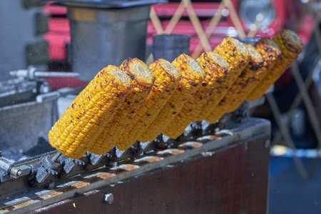 Golden corn on the cob is freshly grilled and displayed at a bustling summer fair, enticing visitors with its delicious aroma and vibrant color.の写真素材
