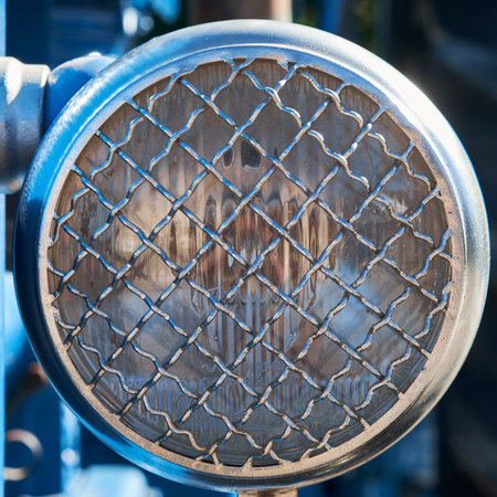 A close-up of a circular, vintage industrial headlight protected by a sturdy wire mesh guard, showcasing rugged design and metallic textures.の写真素材