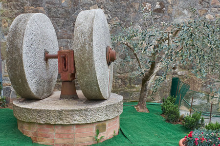Two large, weathered gray stone mill wheels with a rusted red central mechanism, displayed outdoors...