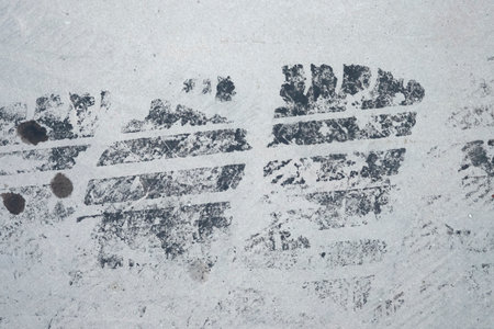 A clear, horizontal tire track impression with specks of dirt and oil on a light gray, dusty...