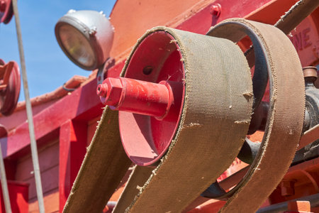 A close-up of a vibrant red industrial pulley and a weathered fabric drive belt on a machine, set...