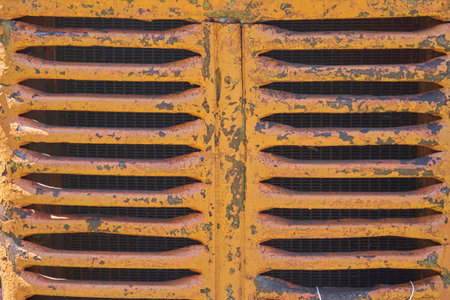 A close-up of a heavily weathered and peeling yellow industrial grille with horizontal slats and a...