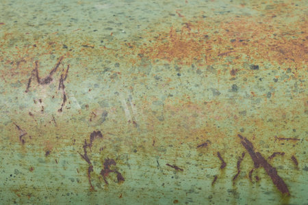 A textured close-up of an aged green painted metal surface, speckled with reddish-brown rust and showing signs of wear, suitable for distressed or industrial backgrounds.の写真素材