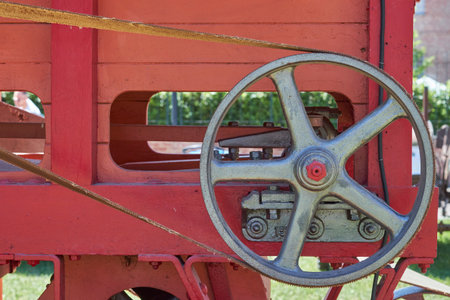 A wide shot of a grey, spoked industrial pulley with a visible drive belt, mounted on a vibrant red farm machine. The scene suggests a powerful, well-maintained agricultural or vintage industrial setting.の写真素材