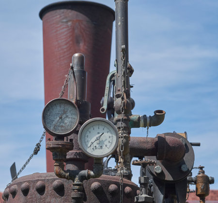 A close-up of a weathered, rusty industrial machine with pipes, chains, and two pressure gauges...