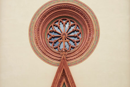 Close-up of a beautiful rose window featuring intricate stone tracery and a central cross, set within a decorative circular frame on a church facade.の写真素材