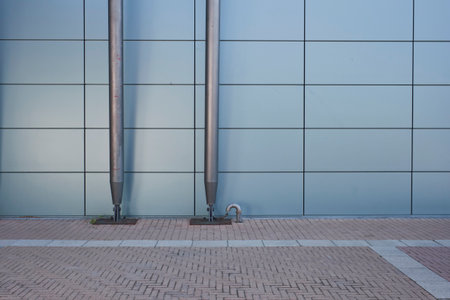 Abstract view of a contemporary light blue tiled building facade with two metallic poles anchored to...