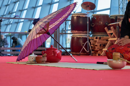 Scene of a Japanese tea ceremony with teapot, cups, a purple parasol, and Taiko drums in the background, captured during a cultural event indoors.の写真素材