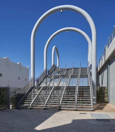 Contemporary metal staircase framed by oversized white arches in a sunny urban setting with...