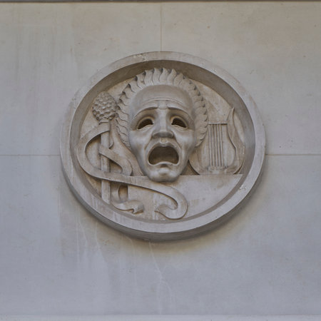 Circular carved stone medallion featuring dramatic mask with open mouth, ornate scrollwork and...