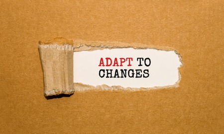 The text ADAPT TO CHANGES appearing behind torn brown paperの写真素材
