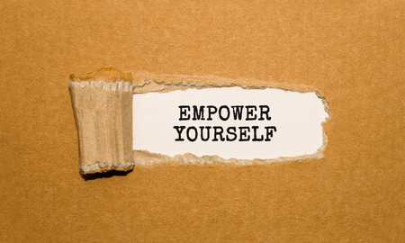 The text EMPOWER YOURSELF appearing behind torn brown paperの写真素材