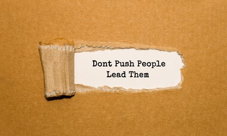 The text Dont Push People Lead Them appearing behind torn brown paperの写真素材