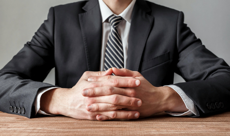 Close up of a businessman at a wooden table with crossed handsの写真素材