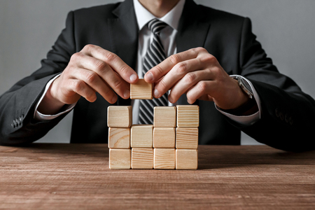 Closeup of businessman making a structure with wooden cubesの写真素材