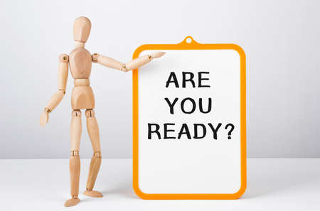 Wooden man shows with a hand to white board with text Are you ready, conceptの写真素材