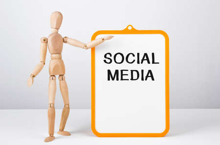 Wooden man shows with a hand to white board with text Social Media, conceptの写真素材