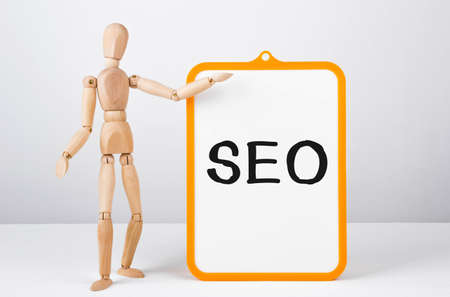 Wooden man shows with a hand to white board with text SEO, conceptの写真素材