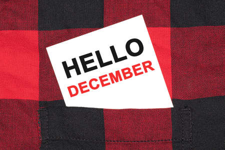 White business card with text HELLO DECEMBER lies in the sleeve of a checkered shirt.の写真素材