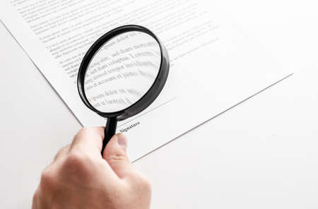 Businessman looking through a magnifying glass to documents.
