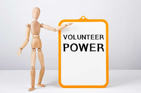 Wooden man shows with a hand to white board with text VOLUNTEER POWER.の写真素材