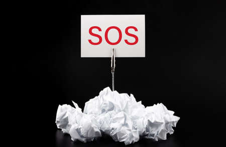 Close-up of crumpled paper on table with text SOS.の写真素材