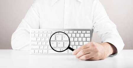 Man with magnifying glass and white keyboard of computer or laptop. Concept of searching web, browsing informationの写真素材
