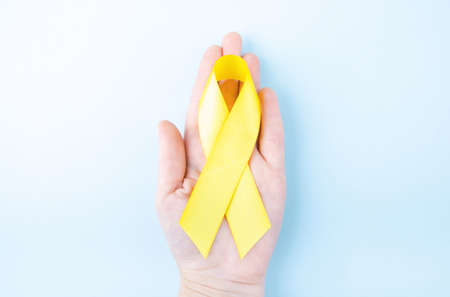 Female hand holding yellow ribbon on blue background. Cancer concept.の写真素材