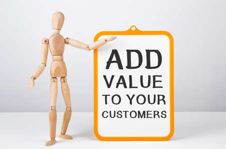 Wooden man shows with a hand to white board with text Add value to your customers.の写真素材