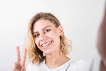Pretty young female with big smile having fun taking light cheerful selfie on white background.
