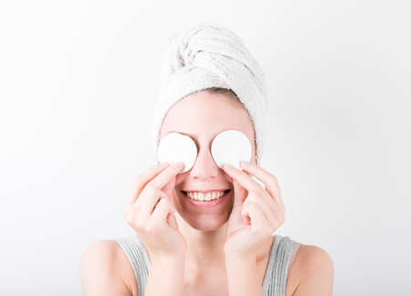 Close up beauty portrait of a smiling attractive woman cleaning her face with a cotton pad isolated over white background.の写真素材