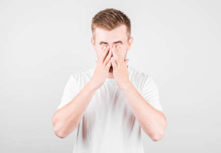 Young handsome man wearing white t-shirt over isolated background tired rubbing nose and eyes feeling fatigue and headacheの写真素材
