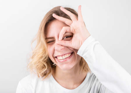 Positive funny female in casual clothes shows ok sign, laughs at camera, demonstrates that...