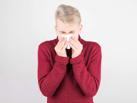A handsome man in a red scarf suffers from a cold and blows his nose into a napkin. The concept of medicine and seasonal colds.の写真素材