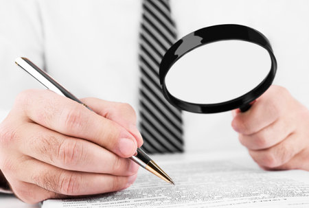 Businessman looking through a magnifying glass to documents.の写真素材
