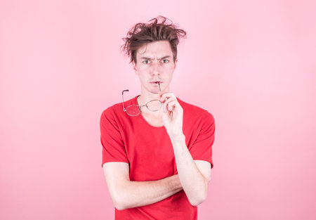 Portrait of a handsome thoughtful man with glasses in his mouth in a casual style of thinking looks...