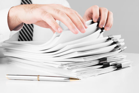 Businessman hands working in stacks of paper files for searching information, business and financial conceptの写真素材