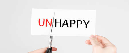 Scissors cutting white paper with the text Unhappy, change word to Happy.