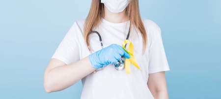 Young female in white t-shirt holding yellow ribbon awareness symbol, sarcoma bone cancer, bladder cancer, liver cancer and childhood cancer concept. Health care.の写真素材