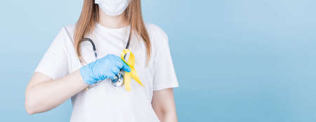 Female doctor holding yellow ribbon awareness symbol for suicide, sarcoma bone cancer, bladder cancer, liver cancer and childhood cancer concept. Health care. Copyspace.の写真素材