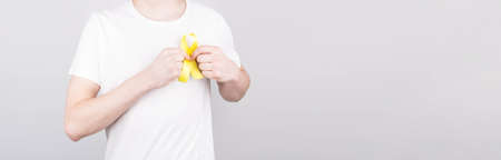 Young man in white t-shirt holding yellow ribbon awareness symbol for suicide, sarcoma bone cancer, bladder cancer, liver cancer and childhood cancer concept. Health care. Copyspace.の写真素材
