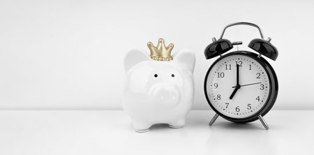 Black alarm clock with piggy bank against a white wall. financial concept.の写真素材