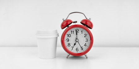 Red alarm clock with coffee cup on white wall backgroundの写真素材