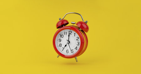 Red alarm clock hangs in the air on yellow backgroundの写真素材