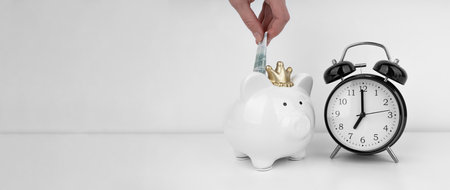 Womans hand put dollar bancnote into a piggy bank with alarm clockの写真素材