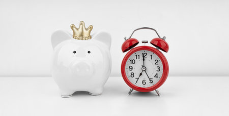 Red alarm clock with piggy bank against a white wall. financial concept.の写真素材