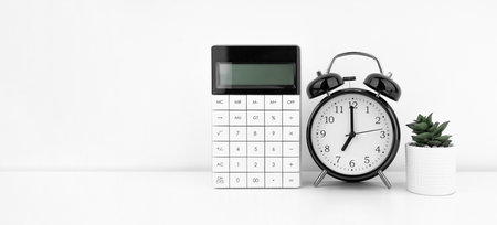 Black alarm clock with calculator against a white wall. financial concept.の写真素材