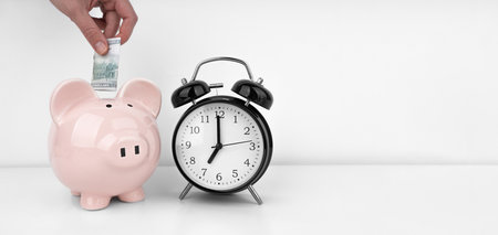 Womans hand put dollar bancnote into a piggy bank with alarm clockの写真素材